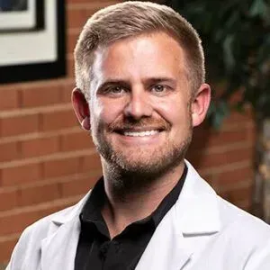 A smiling doctor in a lab coat with a stethoscope around his neck.