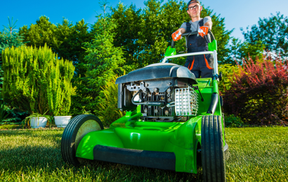 Person mowing a lawn on a bright green riding mower in a sunny garden