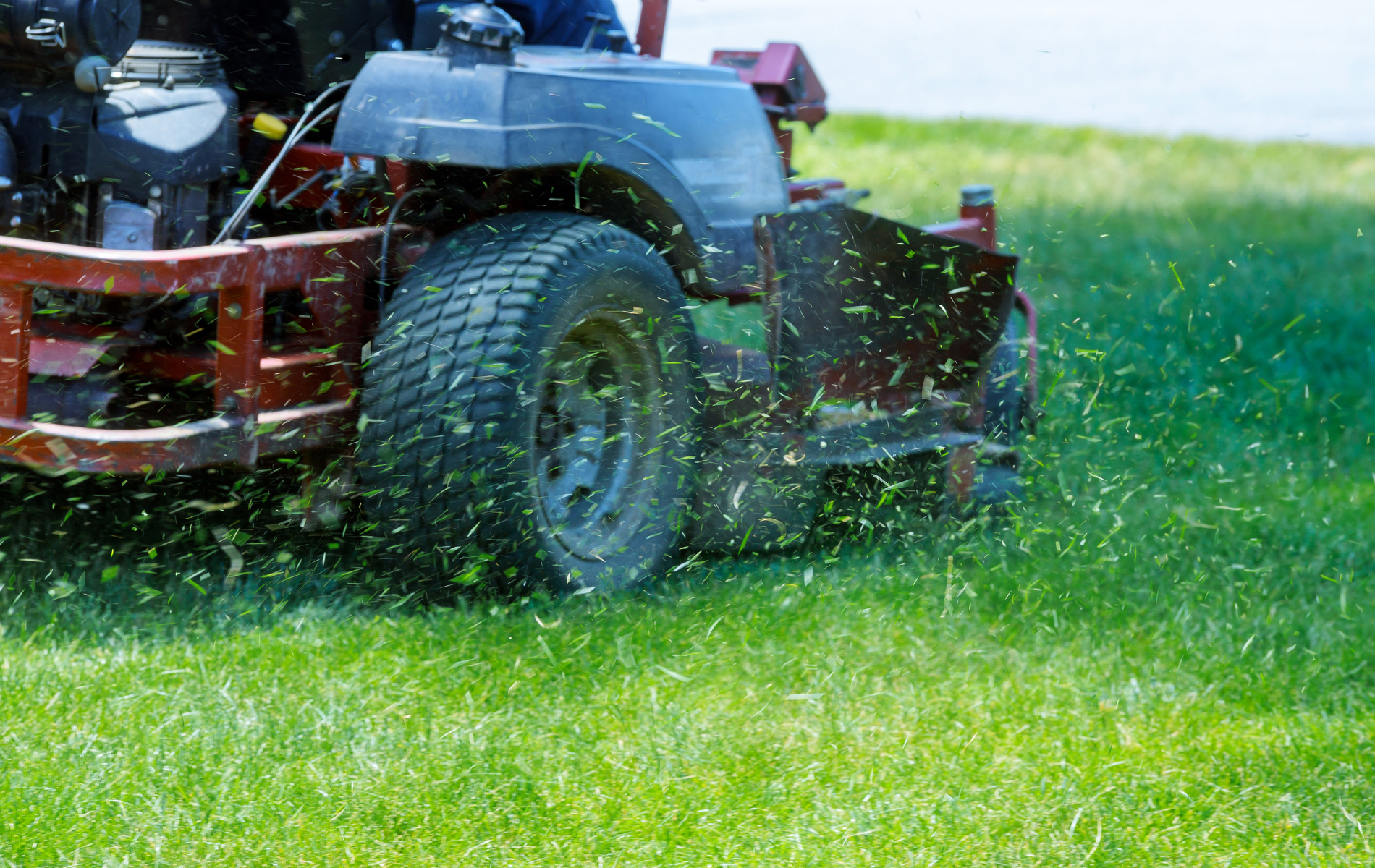 Lawn tractor mowing wet grass, spraying clippings across a green yard