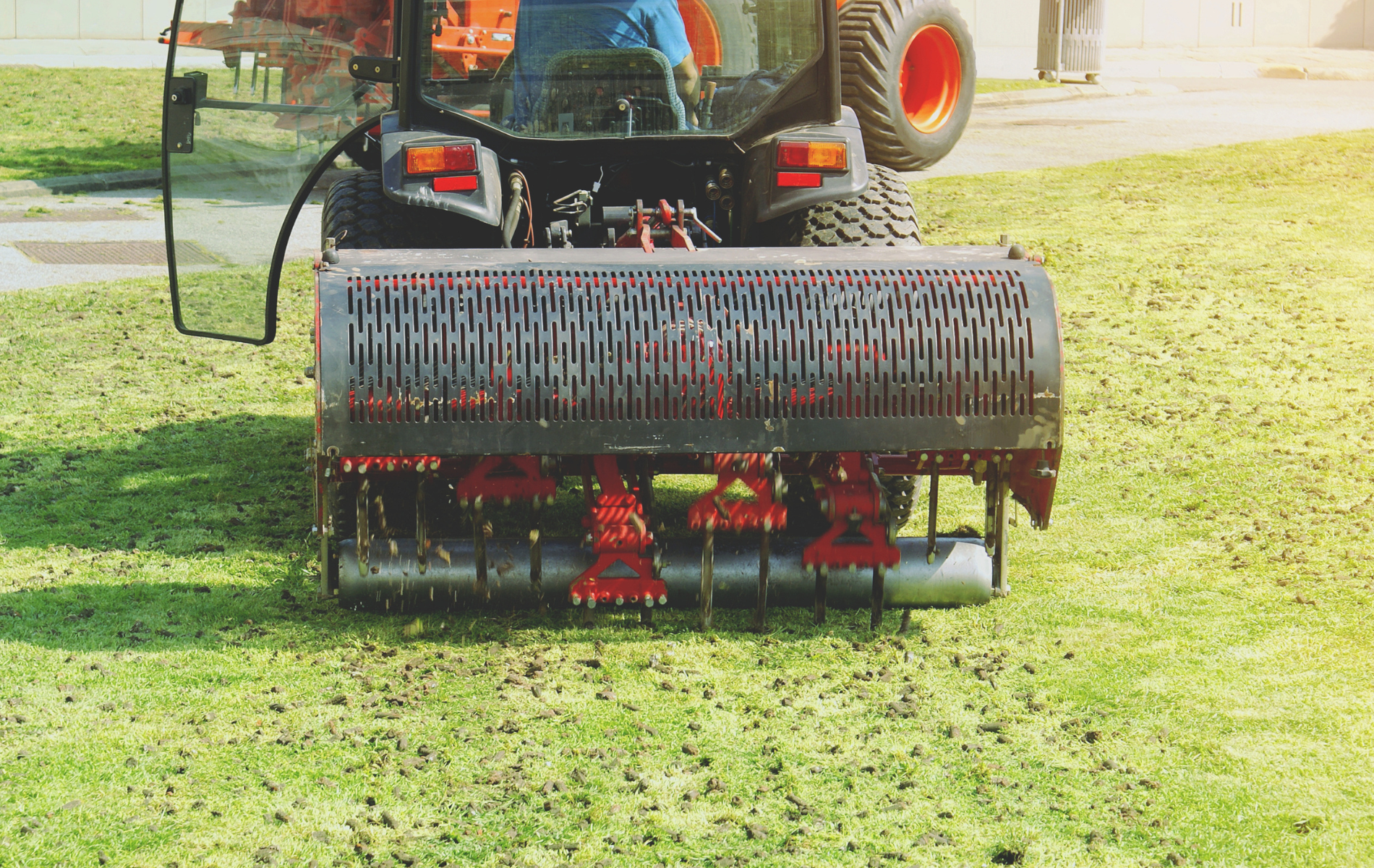 Tractor mowing grass with a rear-mounted red mower attachment in a field