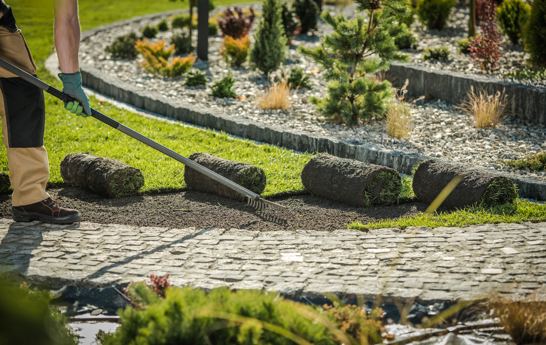Person edging a stone path beside a landscaped garden with a green tool