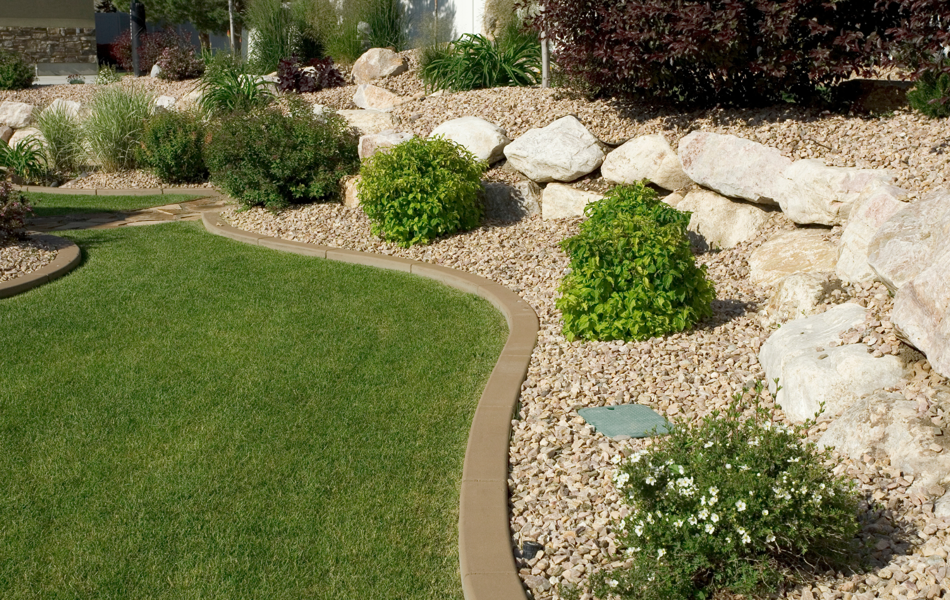 Curved garden edge with green lawn, gravel border, rocks, and small shrubs.