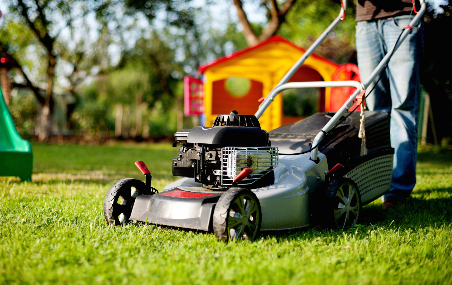Person mowing a green lawn with a push mower in a sunny yard