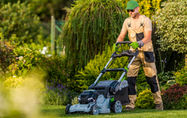 Gardener mowing a lush green lawn with a push mower in a sunny backyard