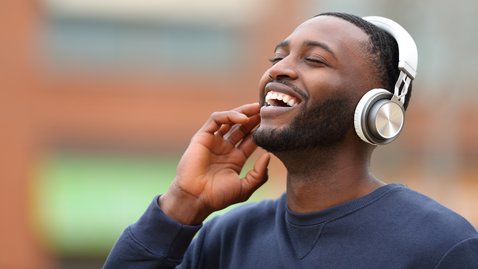 Man with headphones, smiling, listening to music outdoors.