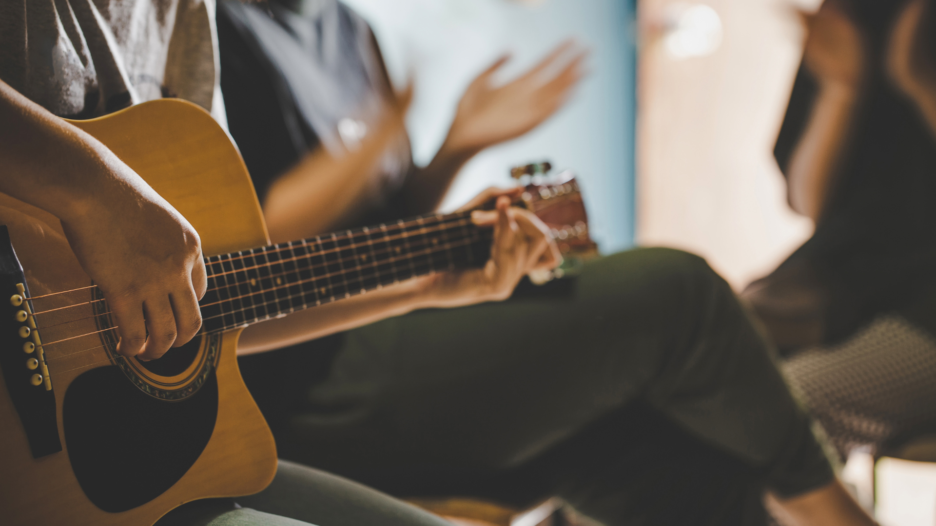 Person playing acoustic guitar; two people clapping in the background.
