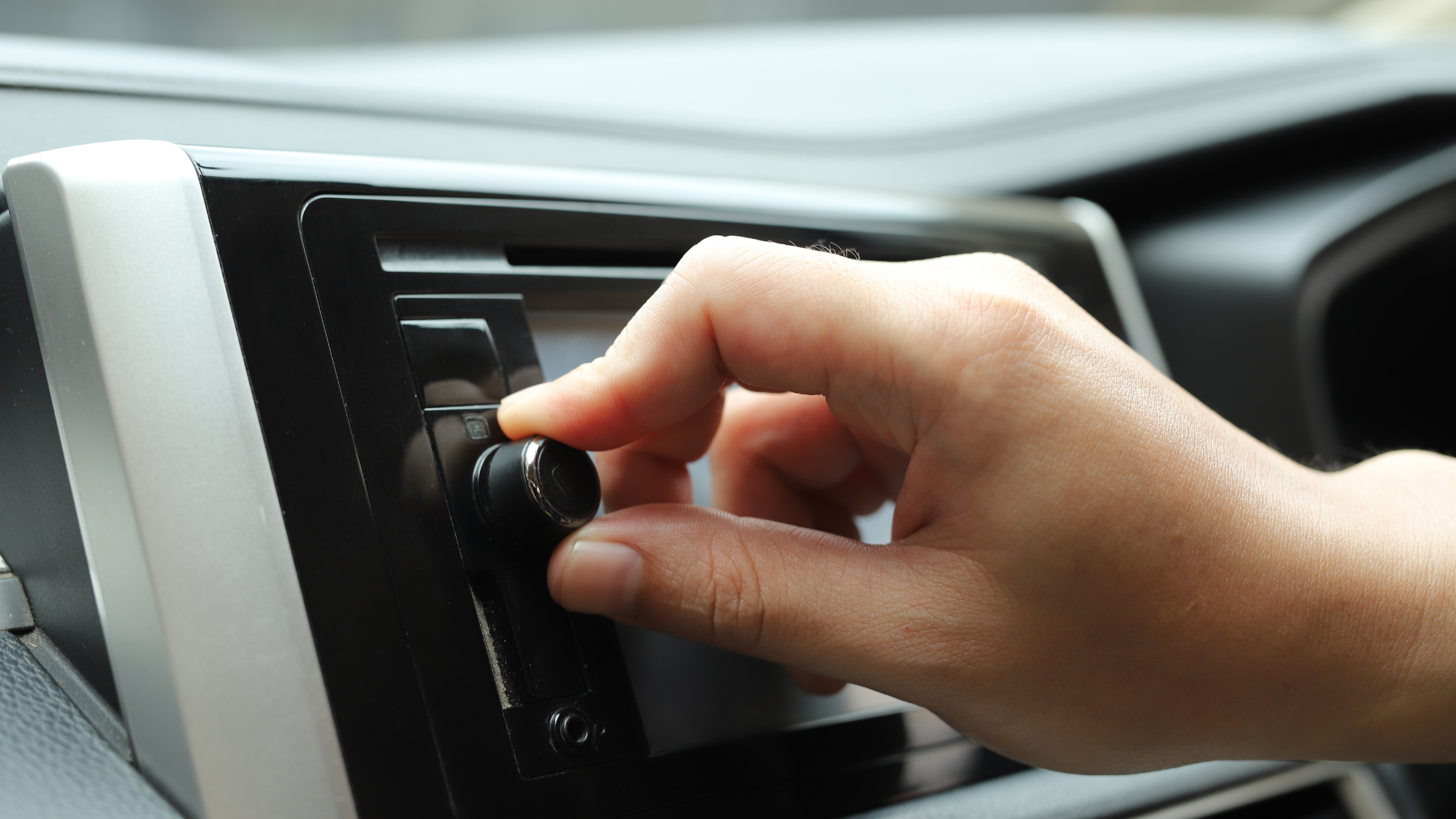 Hand turning a car radio volume knob in a car interior.