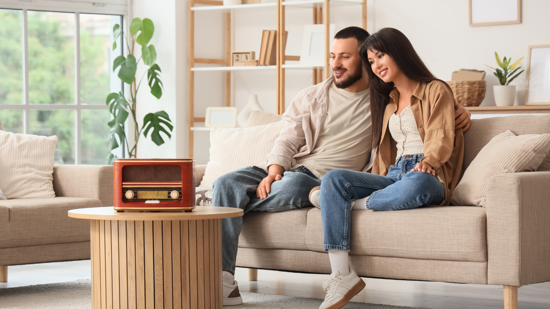 Couple on a sofa listening to a retro radio in a light-filled living room.