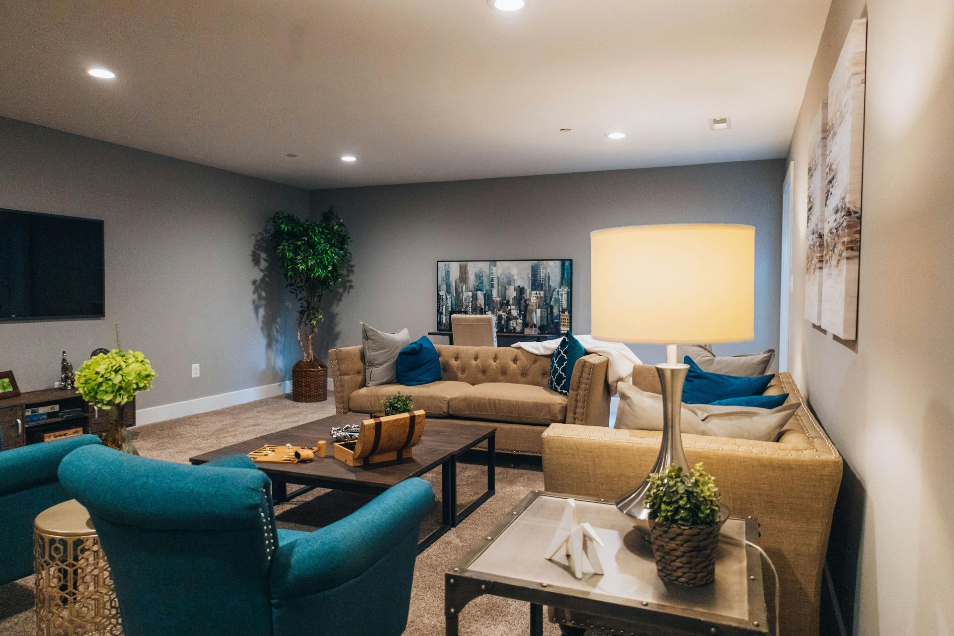 Modern living room with teal chairs, tan sofa, coffee table, wall art, and warm recessed lighting