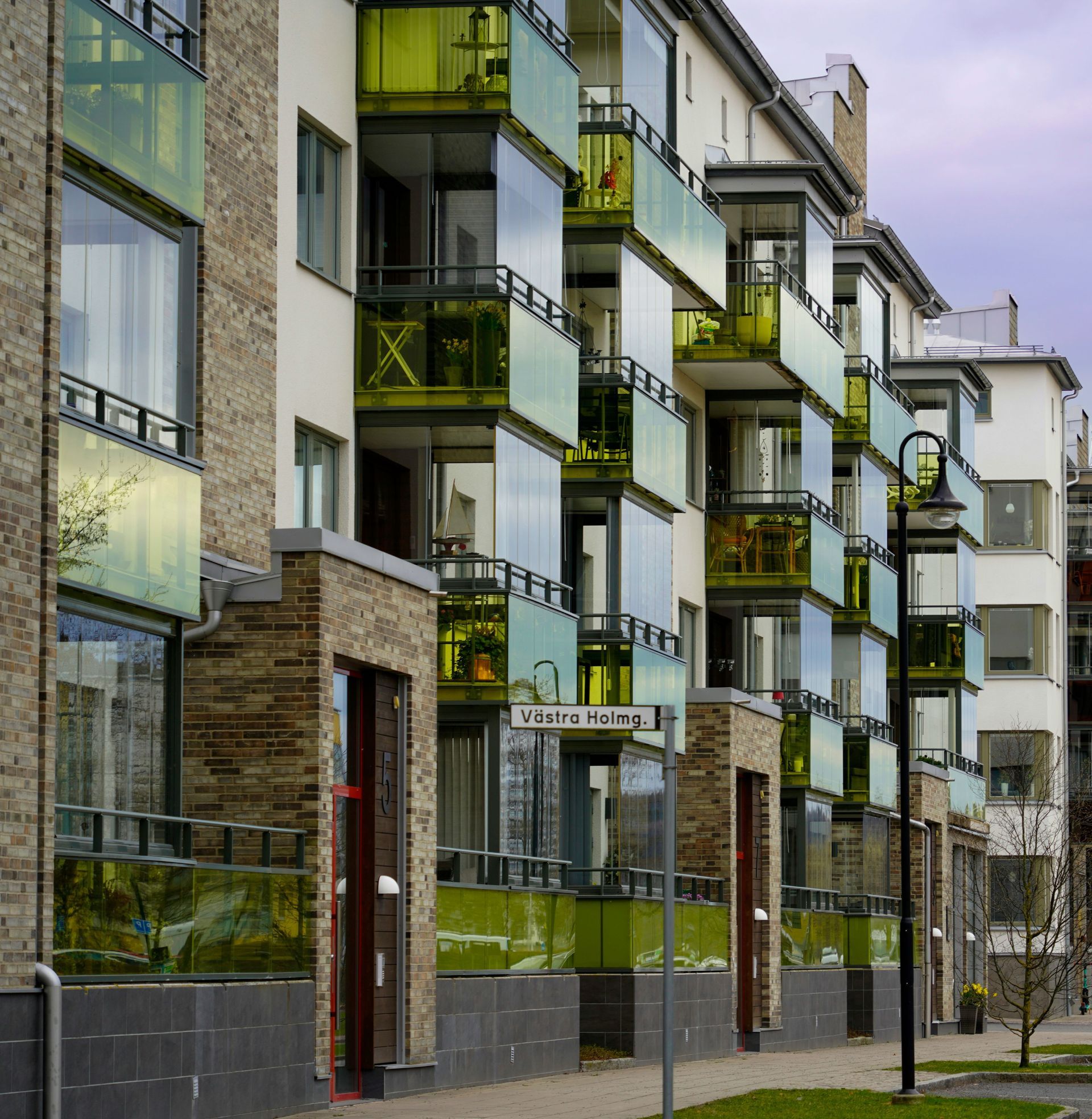 Modern apartment building with glass balconies and green accents along a street