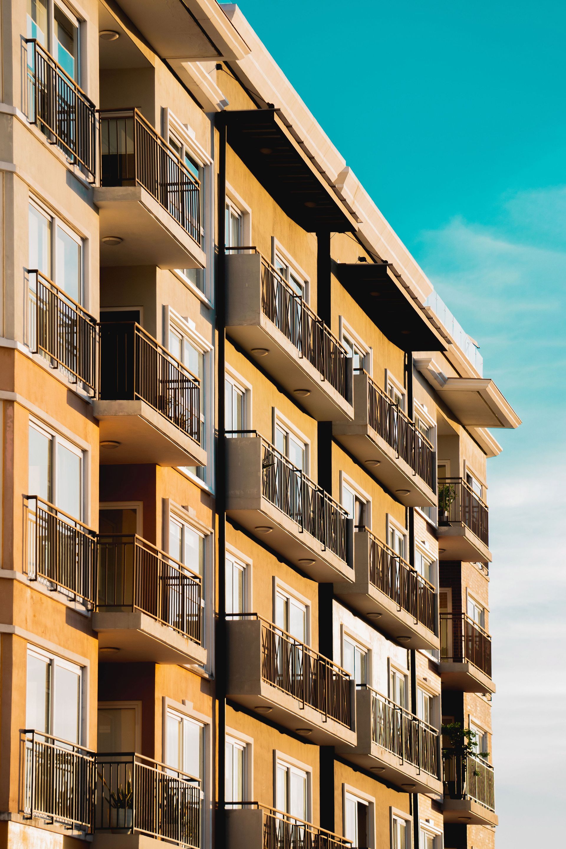 Tall beige apartment building with balconies against a bright blue sky