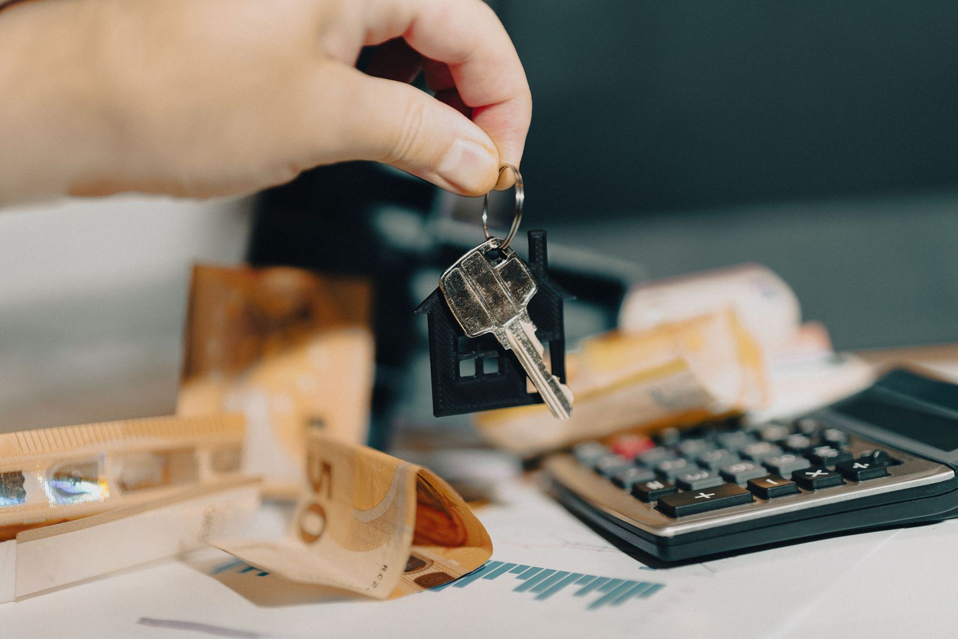 Hand holding car keys above a desk with a calculator and scattered cash bills