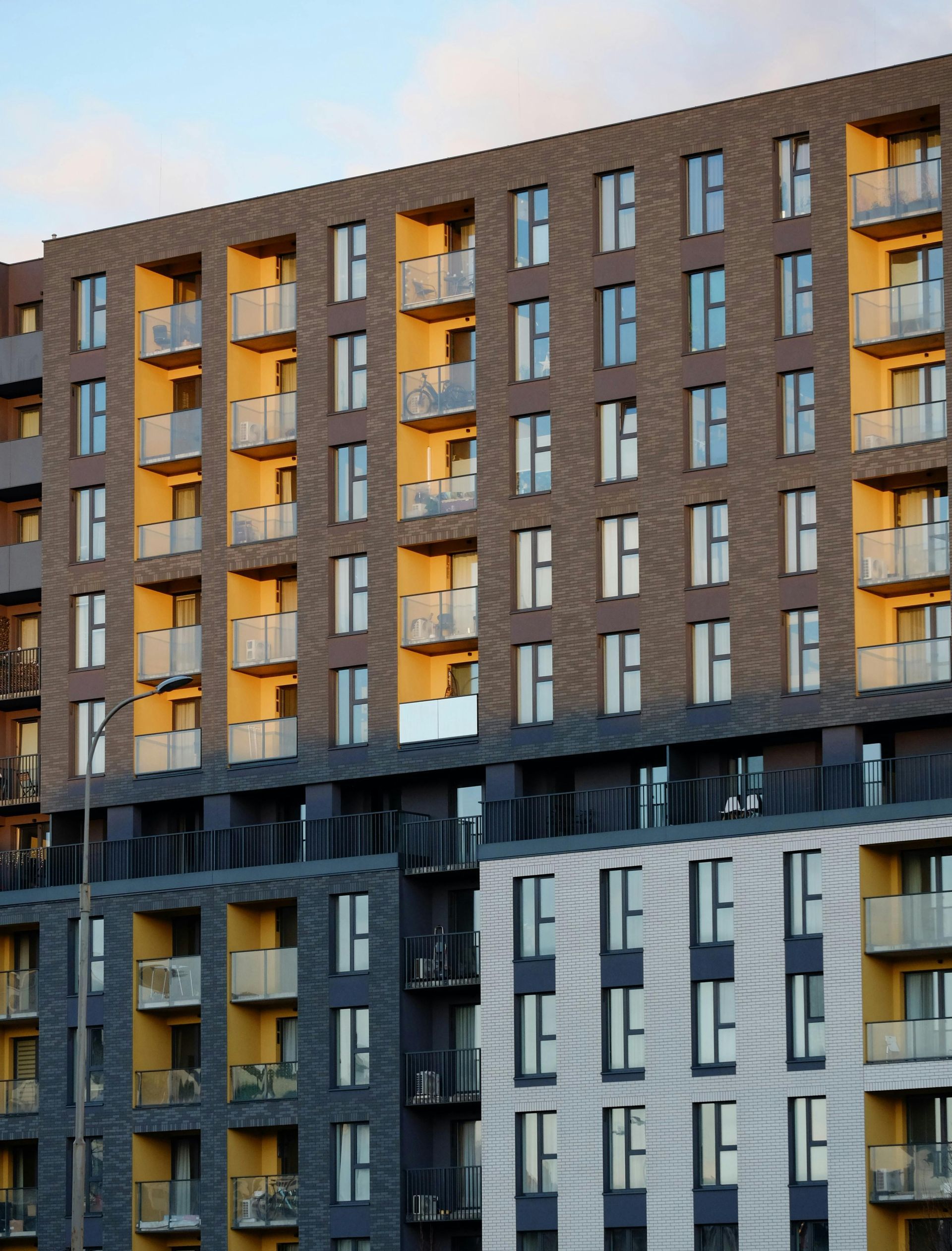 Modern apartment building with brown brick and gray panels, lit windows at dusk.