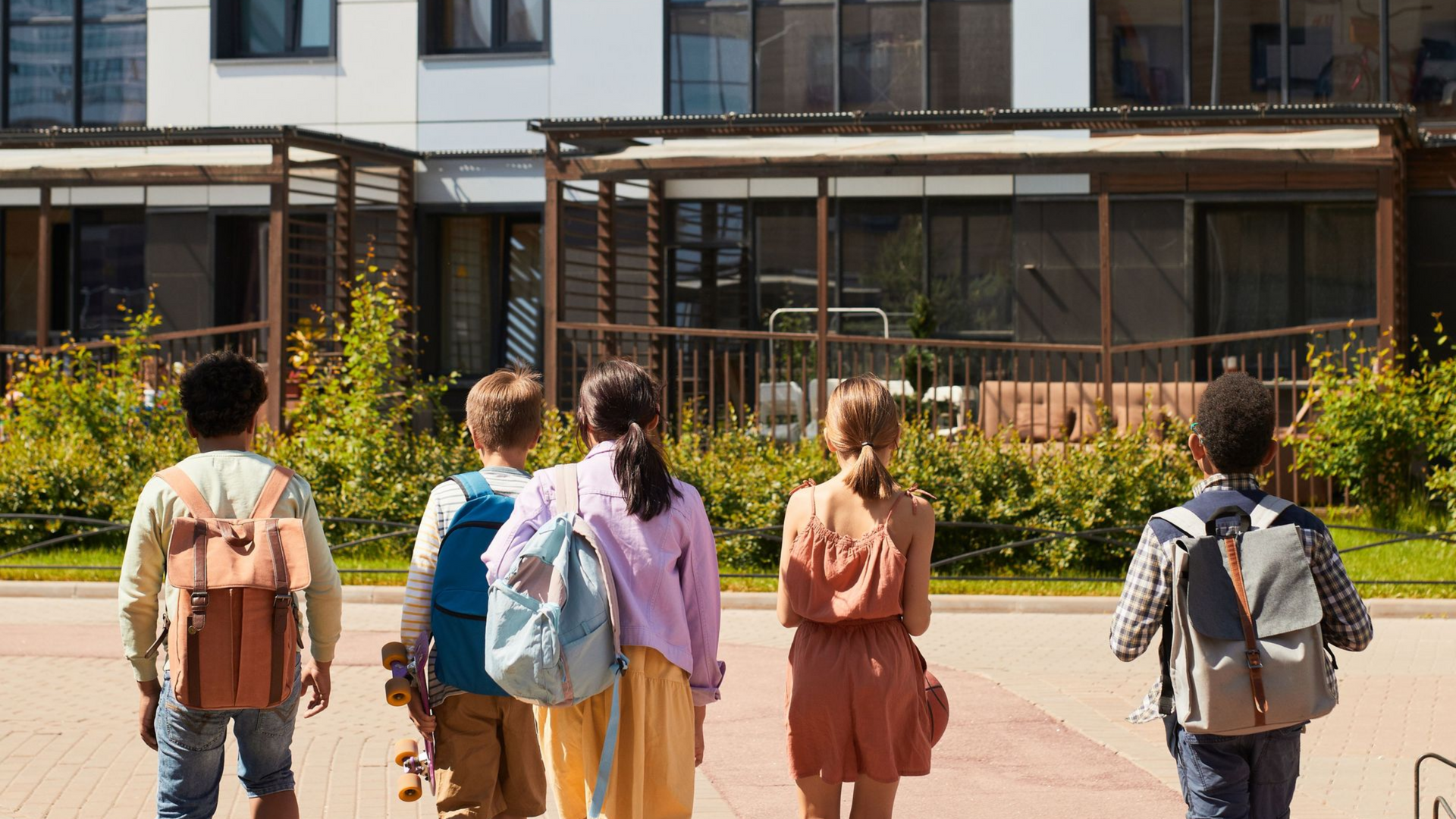 Students walking toward a modern school building, carrying backpacks on a sunny day