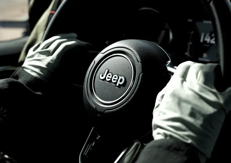 Hands on a Jeep steering wheel inside a dark vehicle interior, black and white gloves visible