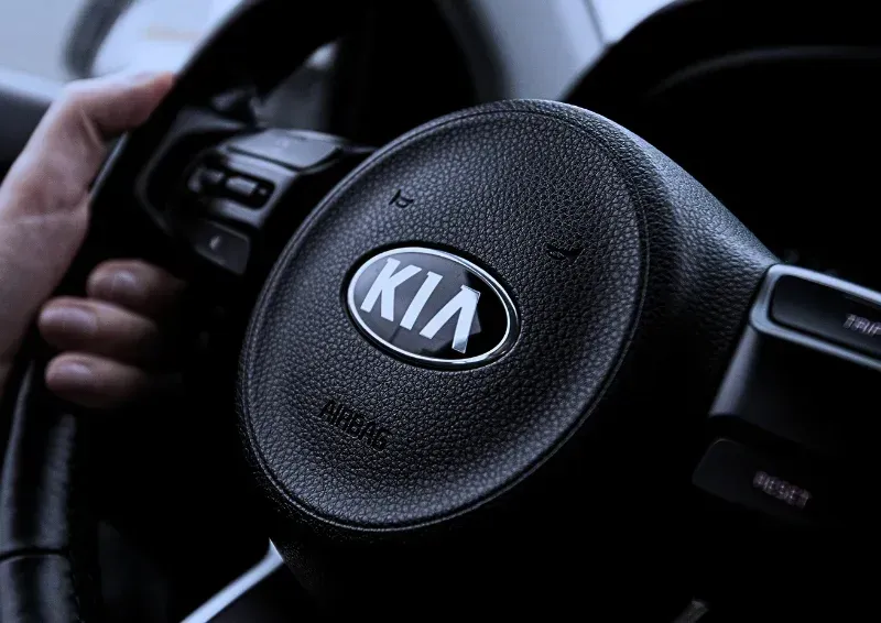 Hands gripping a black Kia steering wheel with chrome logo in a car interior