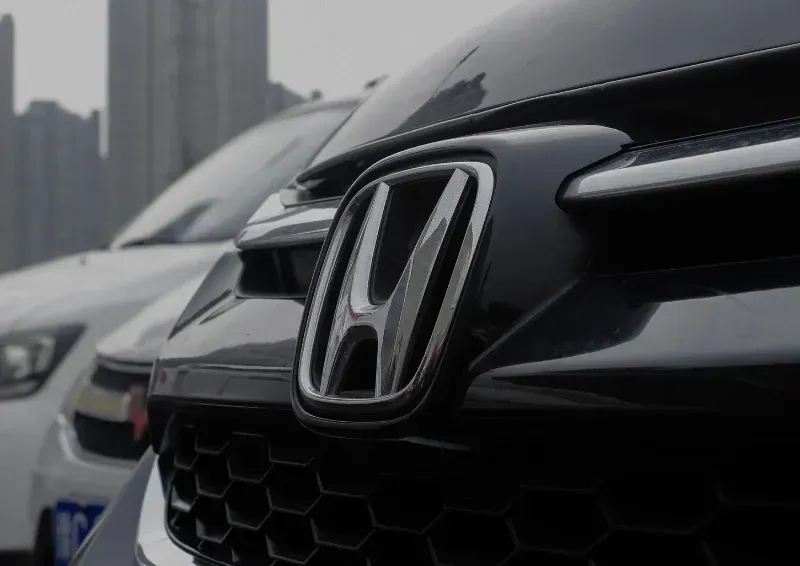 Close-up of a black Honda car grille with logo, parked beside a white vehicle in a city setting
