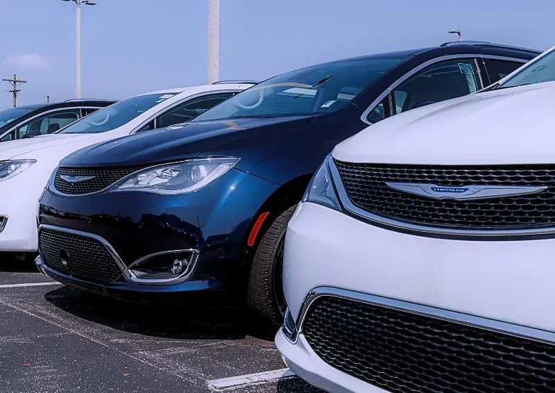 Row of parked cars, including a white car and a blue sedan, in a dealership lot