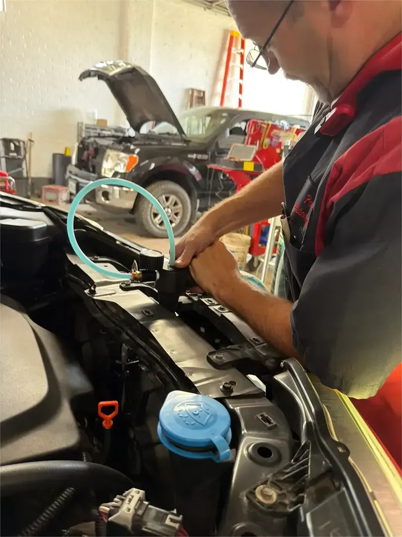 Mechanic working on a car engine with the hood open, showing the radiator and battery area
