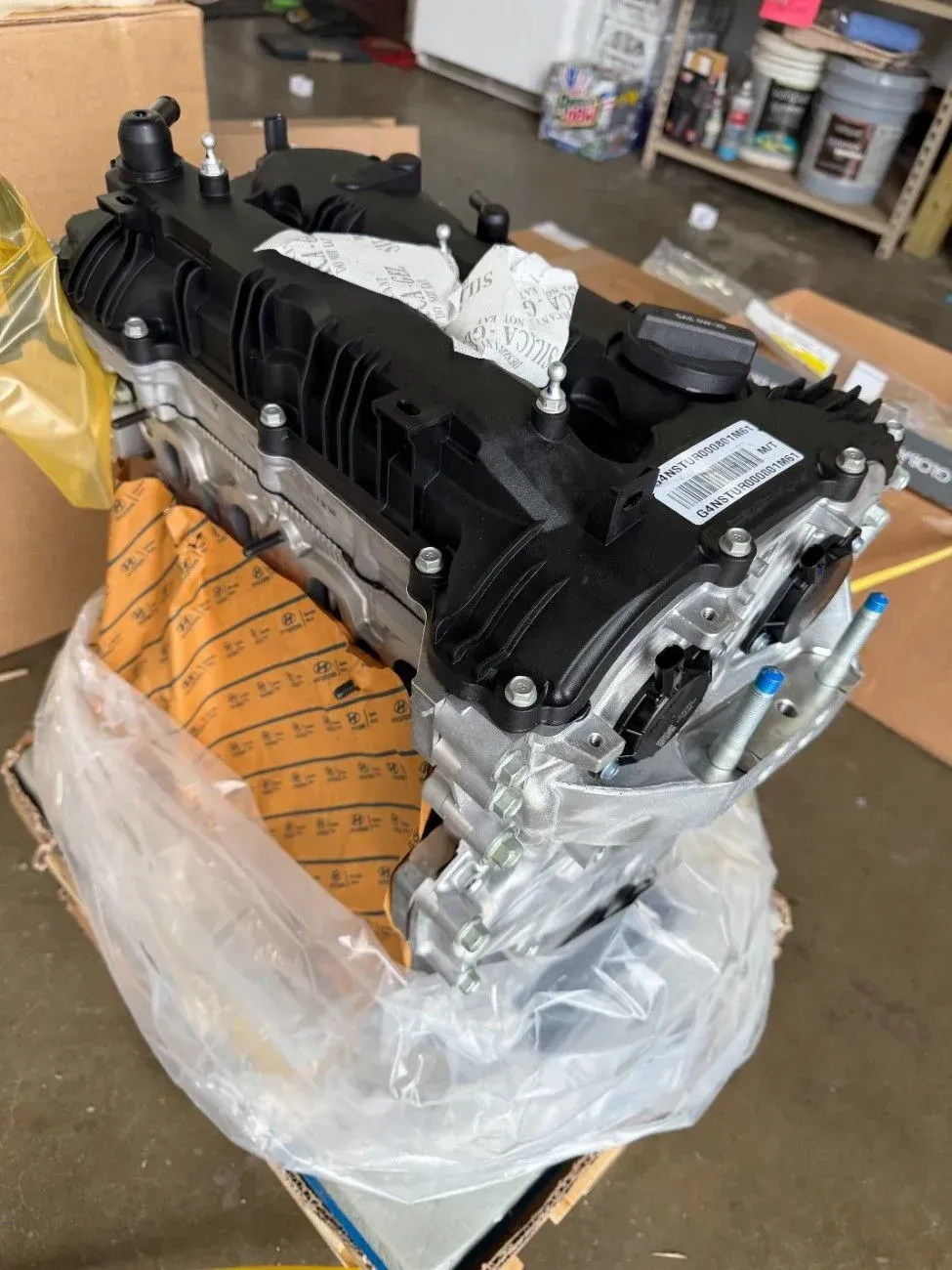 Black engine on a pallet wrapped in plastic inside a workshop or garage