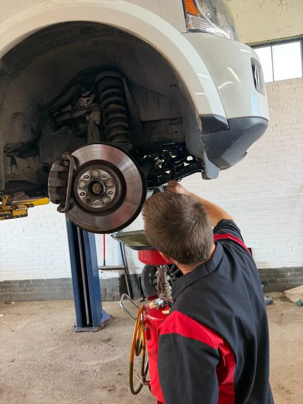 Mechanic working under raised car, inspecting front wheel and suspension in a garage