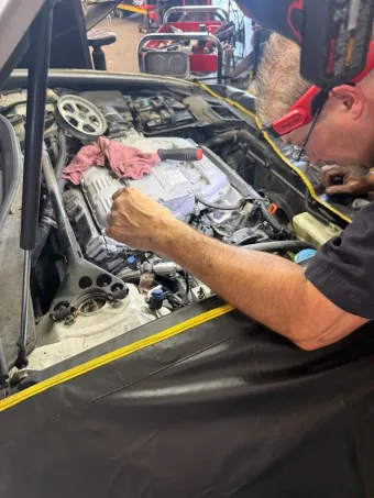 Mechanic in Cape Girardeau, MO working on a race car engine in a garage, with tools and red safety gear nearby