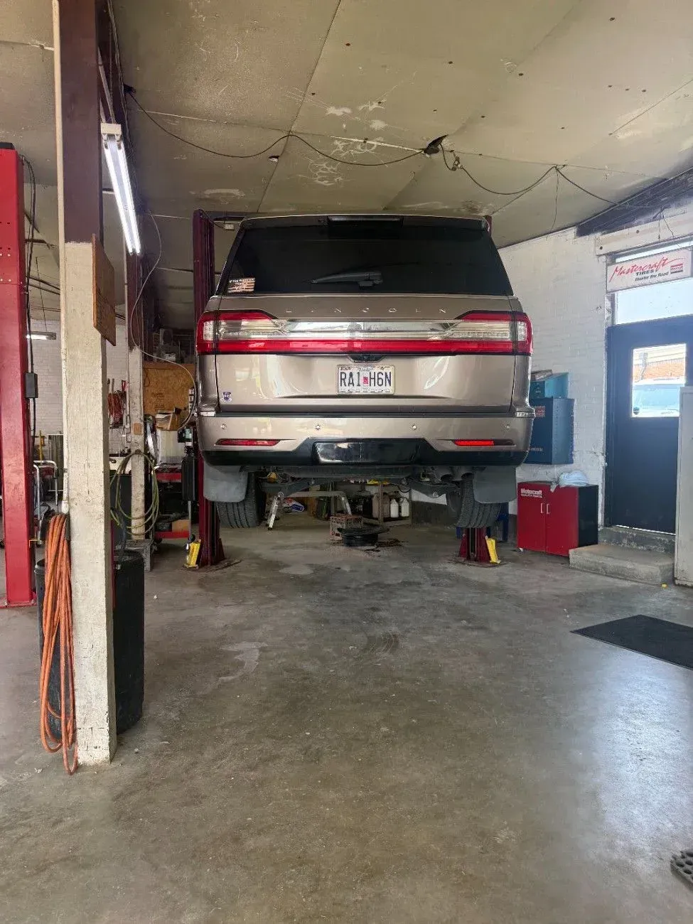 SUV parked on jack stands inside a cramped garage, viewed from the rear.