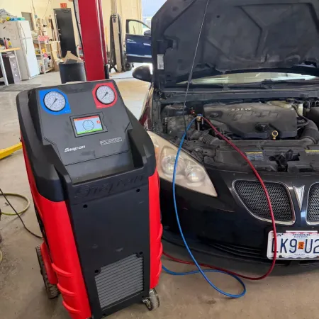 Car AC service machine with gauges connected to a black car in a garage, hood open