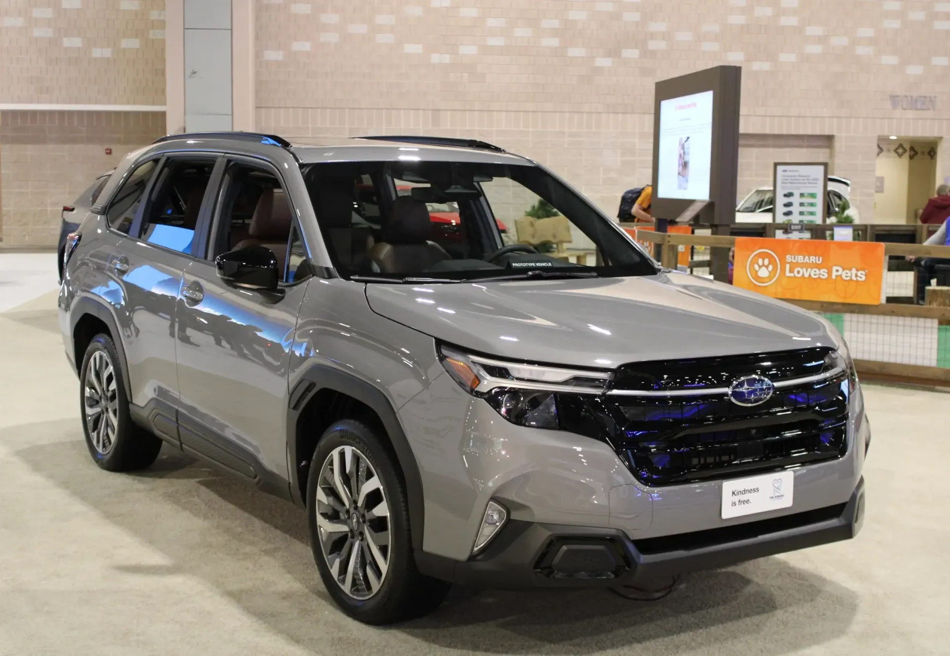 Gray SUV on display in a showroom, angled front view with orange signage in the background