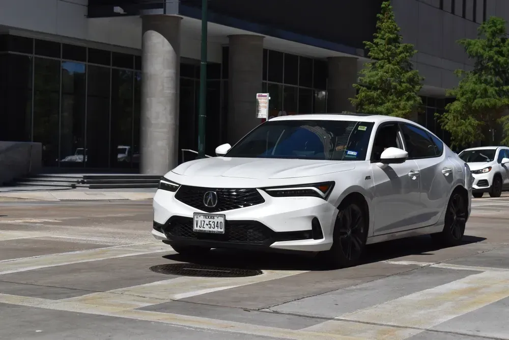 White sedan parked on a city street in front of a modern office building.