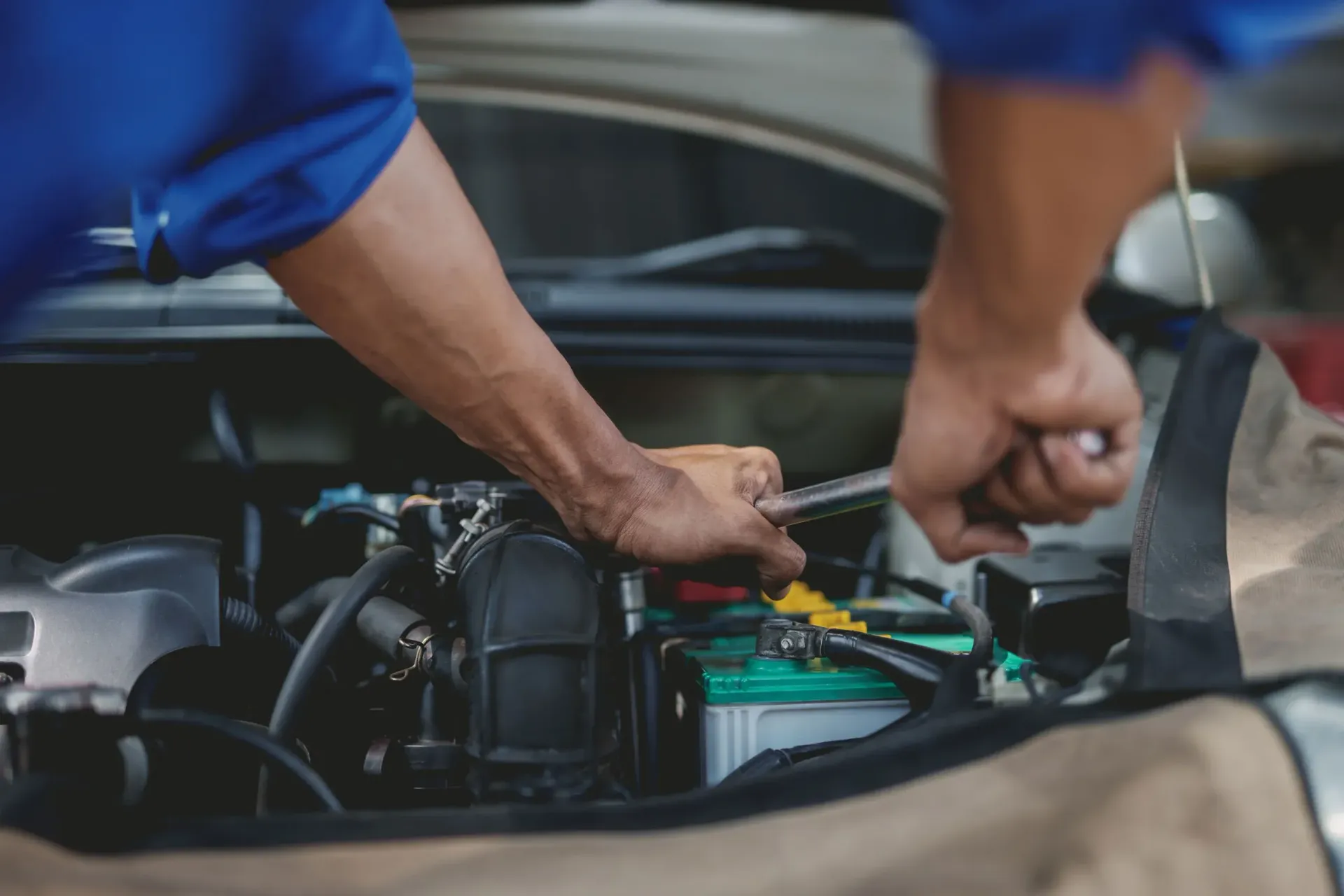 Hands working on a car engine in a garage, adjusting green battery cables under the hood in Cape Girardeau, MO