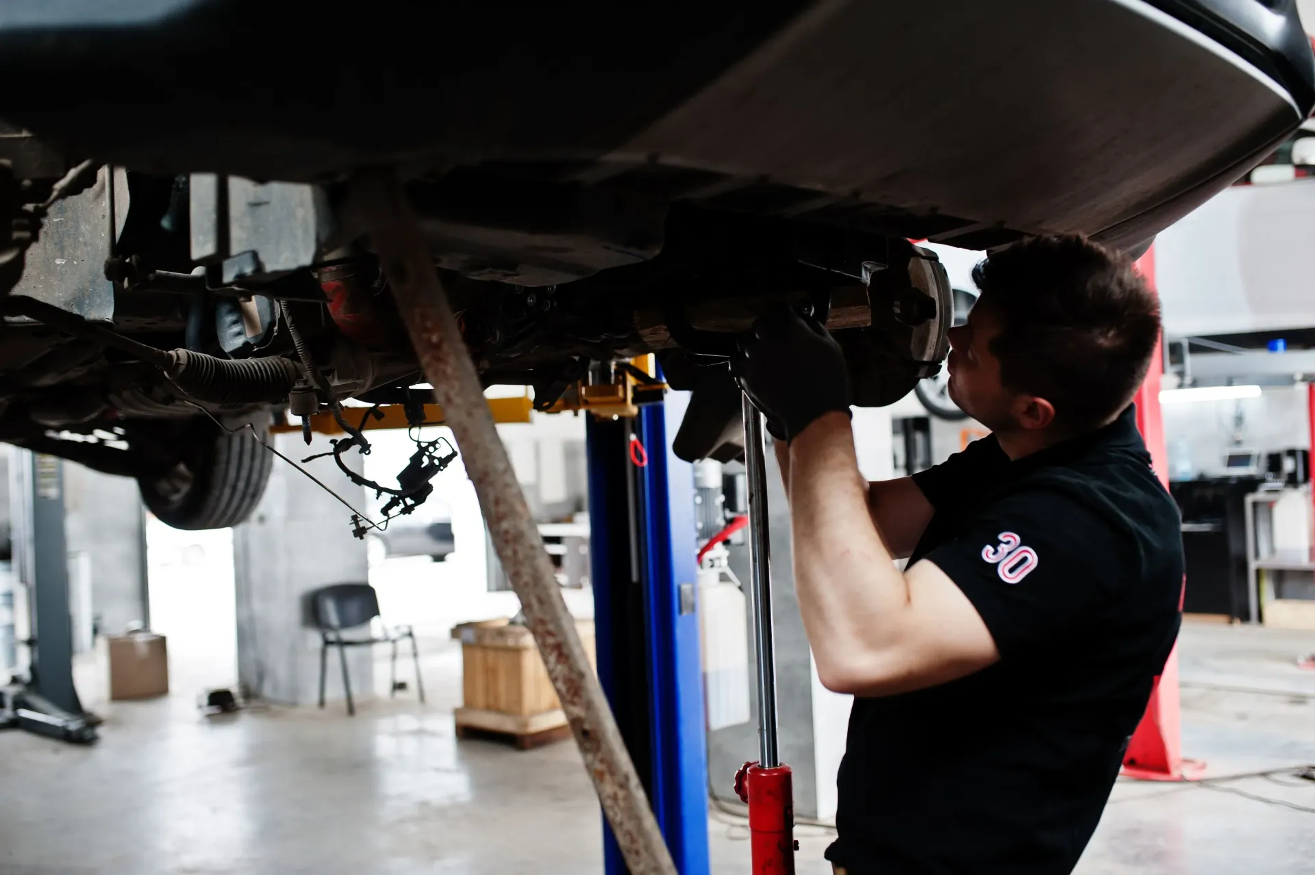 Mechanic working under a raised car in a garage, using tools to inspect the underside in Cape Girardeau, MO