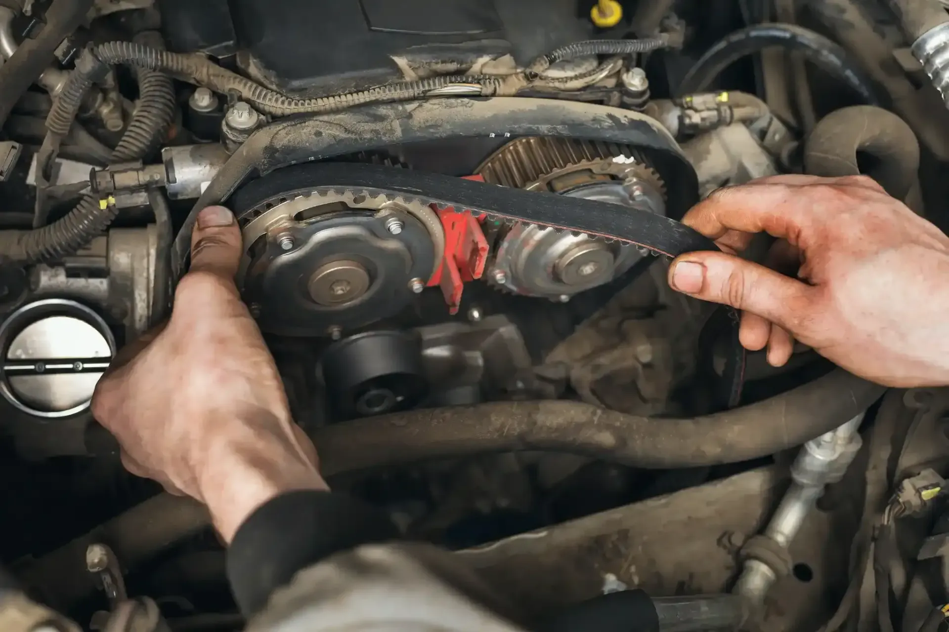 Hands working on a car engine, holding a timing belt near red-marked pulleys.