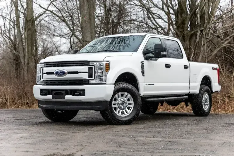 White Ford Super Duty pickup truck parked on a gravel road in a wooded area