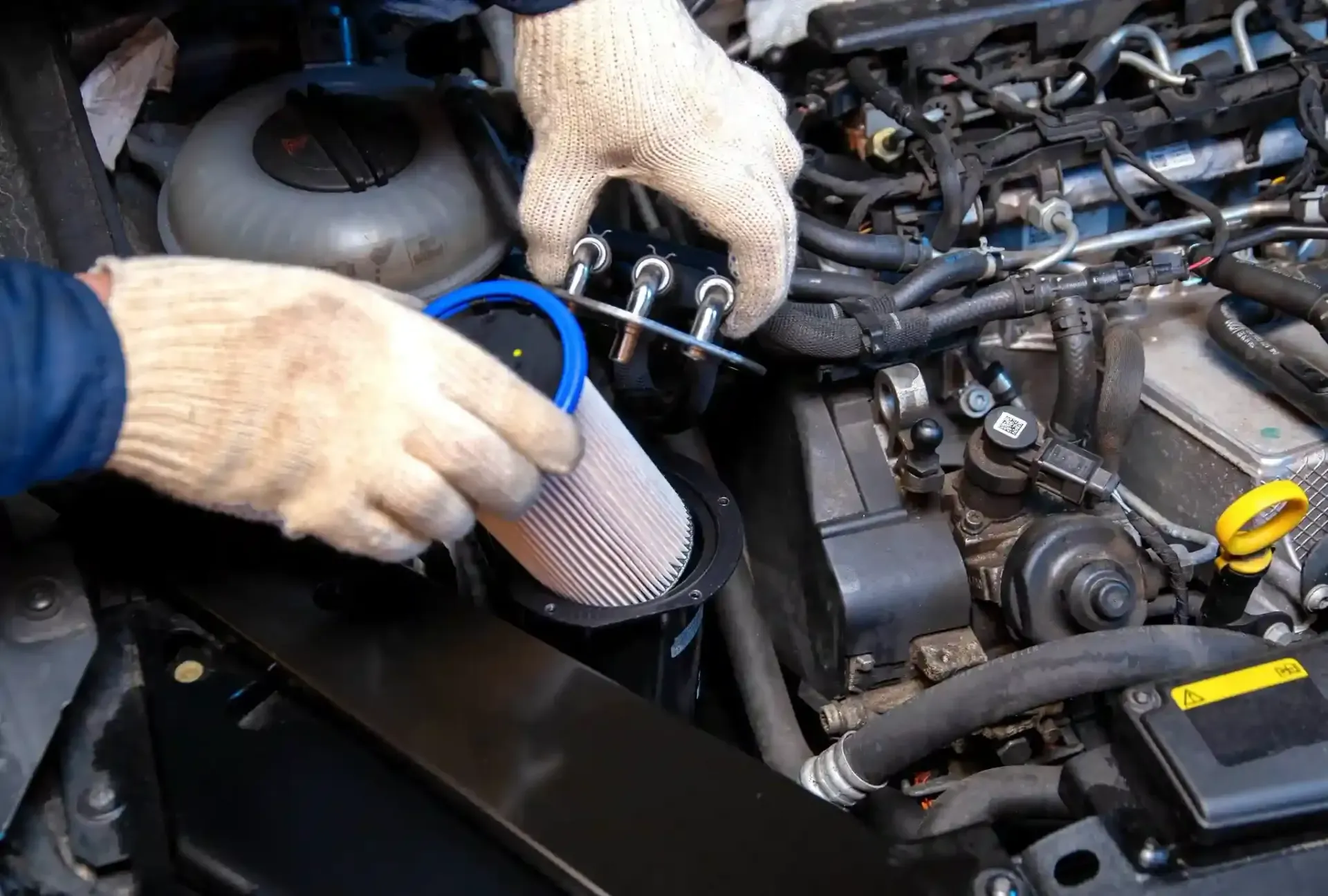 Gloved hands working on a car engine, holding a blue funnel over the intake area in Cape Girardeau, MO