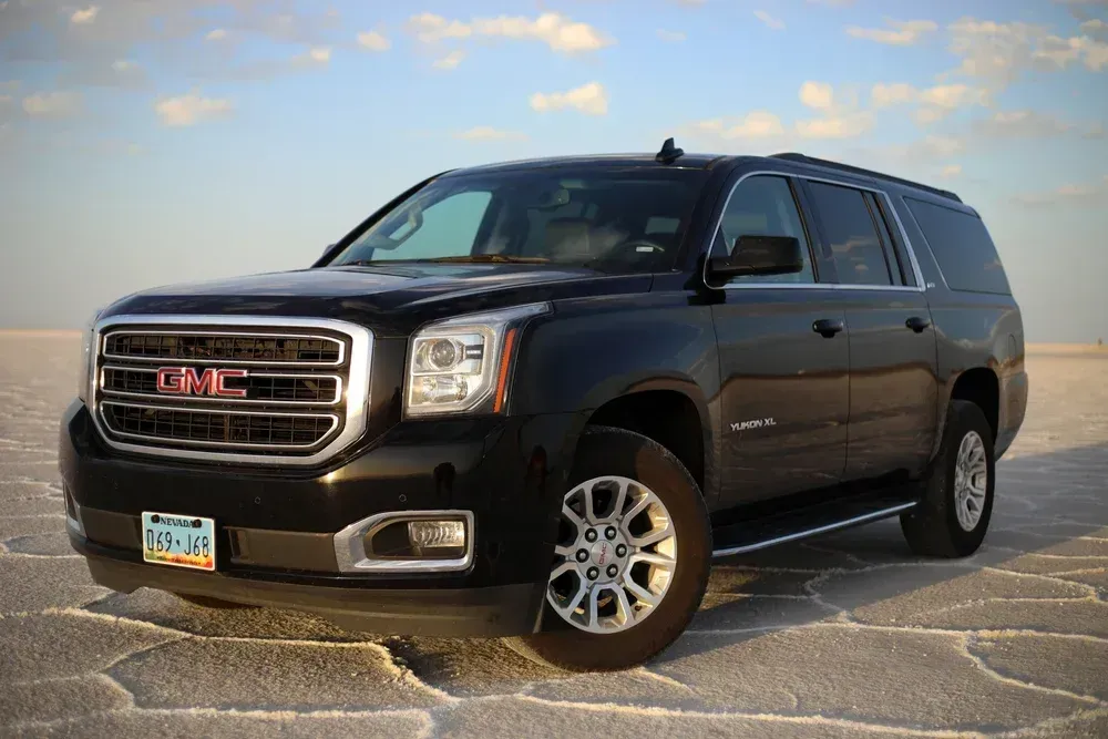 Black GMC SUV parked on a stone overlook by the water at sunset