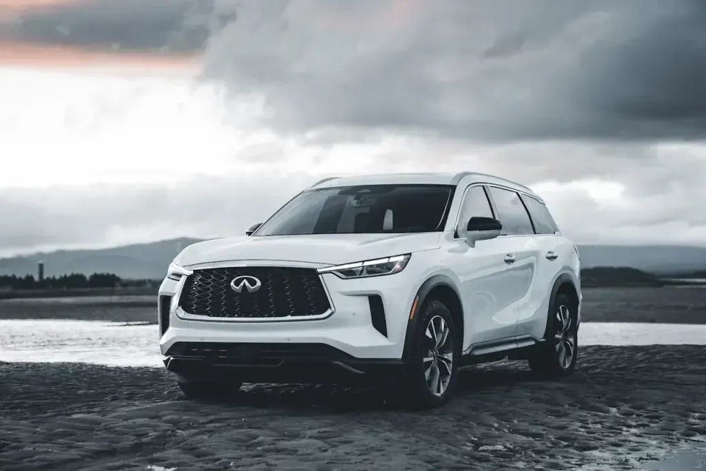 White SUV parked on a wet road beside water under cloudy skies