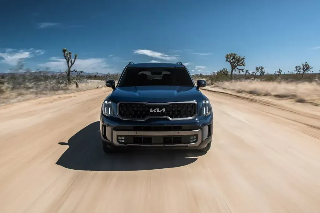 Blue SUV driving on a dusty desert road under a clear sky