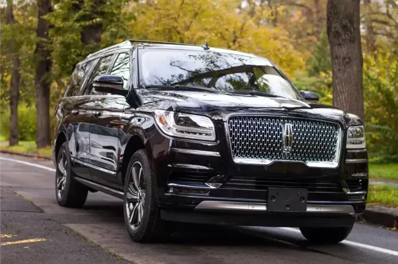 Black luxury SUV driving on a tree-lined road in autumn
