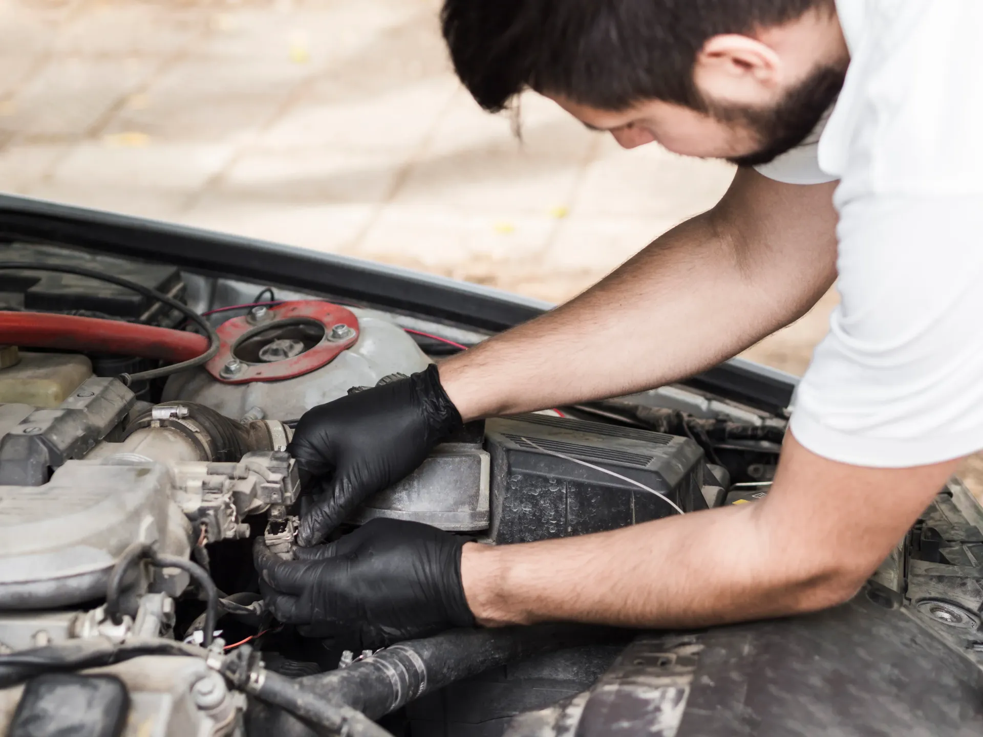 Mechanic wearing black gloves works on a car engine with the hood open