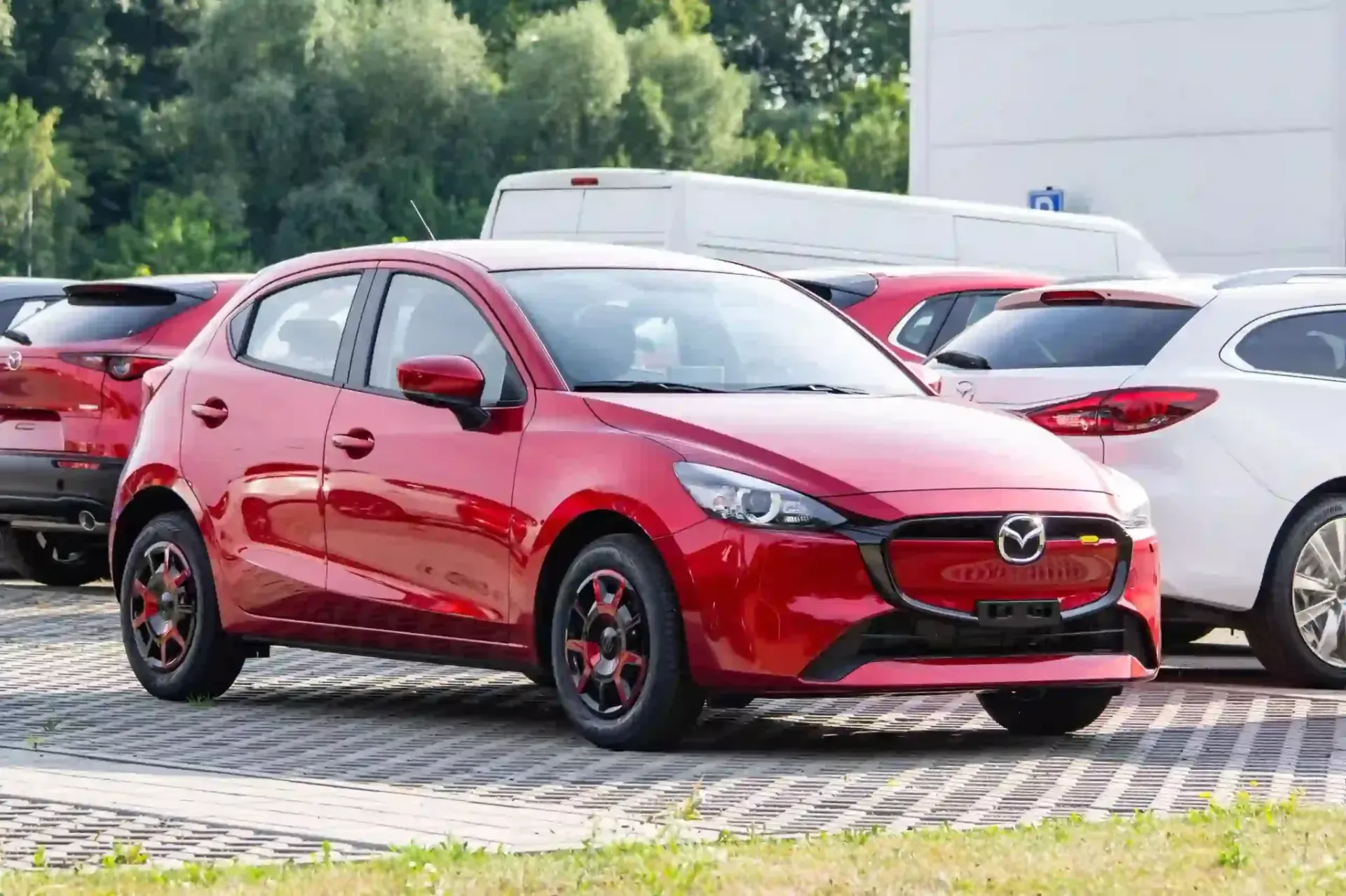 Red Mazda hatchback parked outdoors among other cars, front-left view