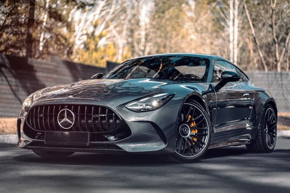 Gray Mercedes sports coupe parked on a road with blurred trees in the background