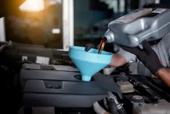 Gloved hands pour oil into a car engine through a blue funnel in a garage in Cape Girardeau, MO