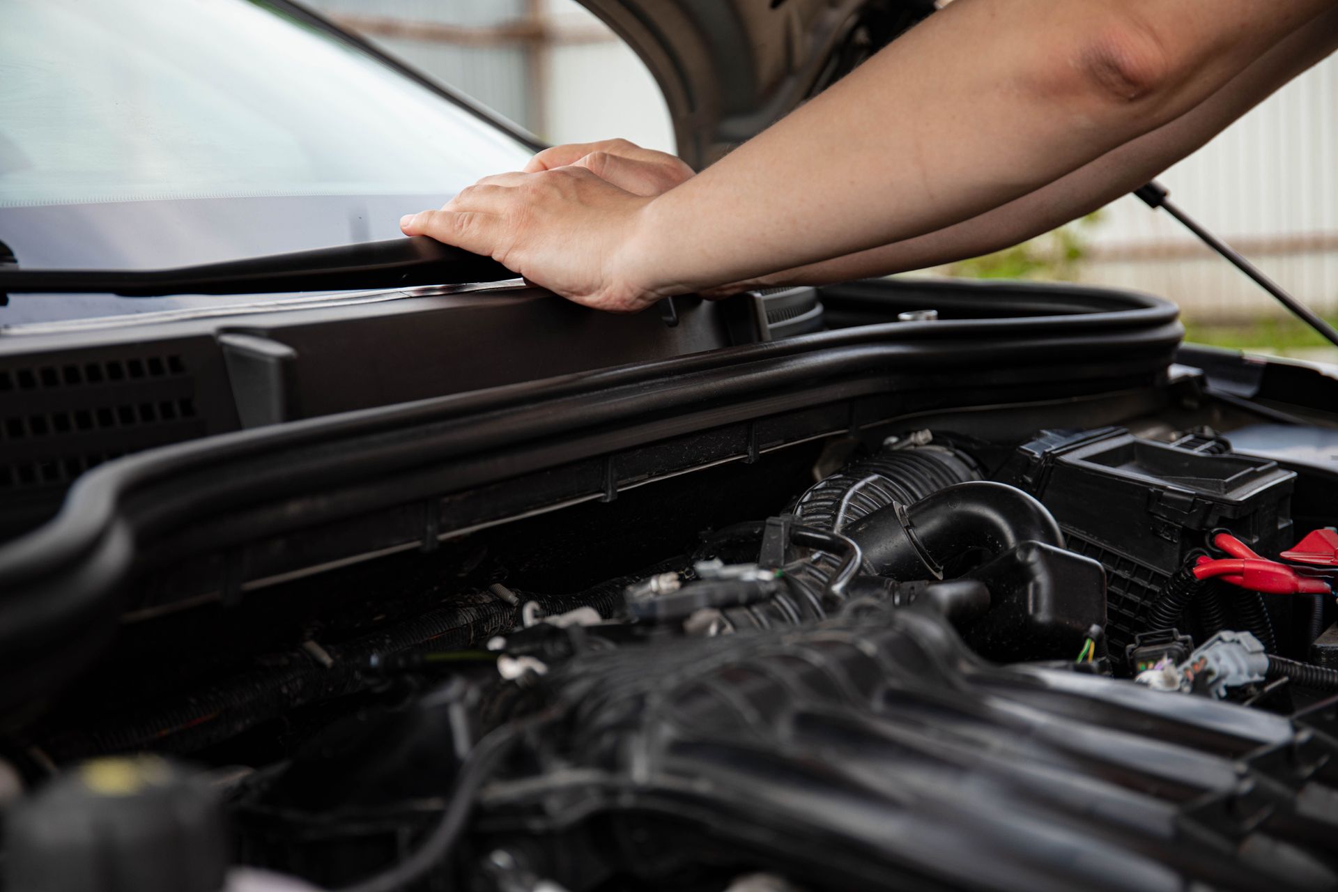 Hands working under a car hood in an engine bay