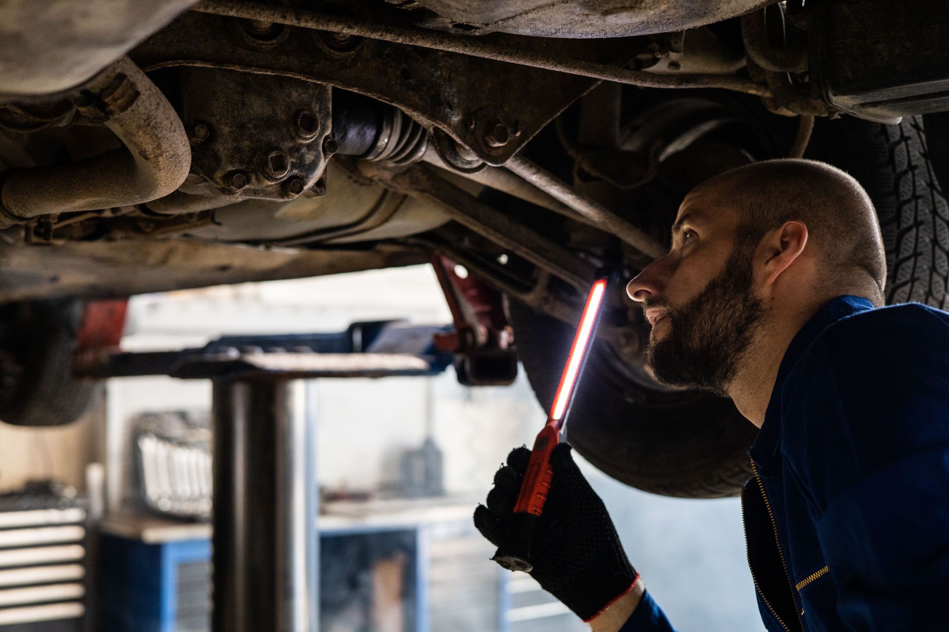 Mechanic inspecting the underside of a car with a flashlight in an auto shop