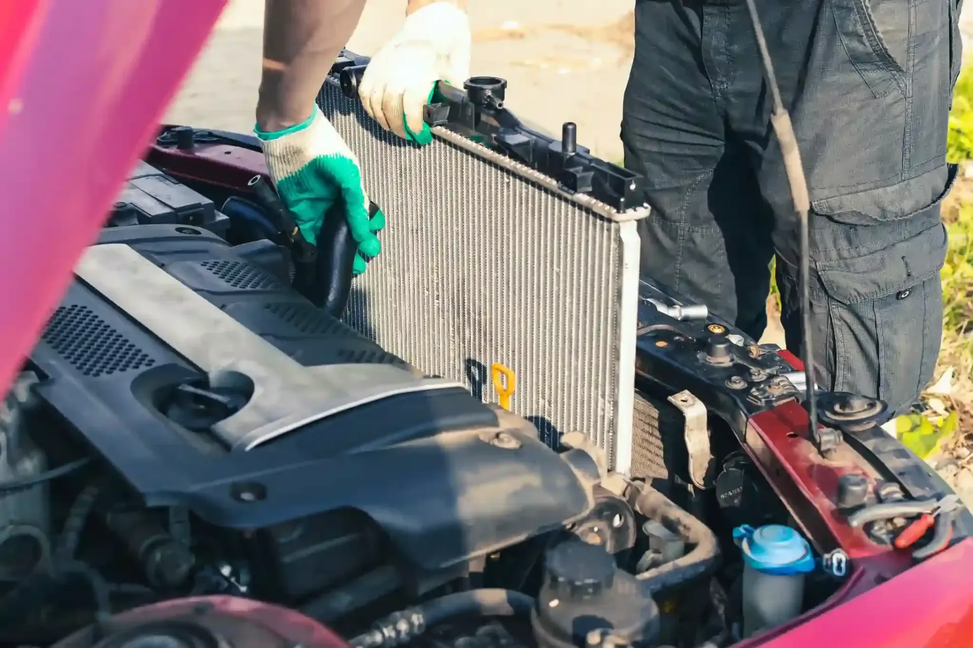 Mechanic working on a car engine with the hood open, showing the radiator and battery area