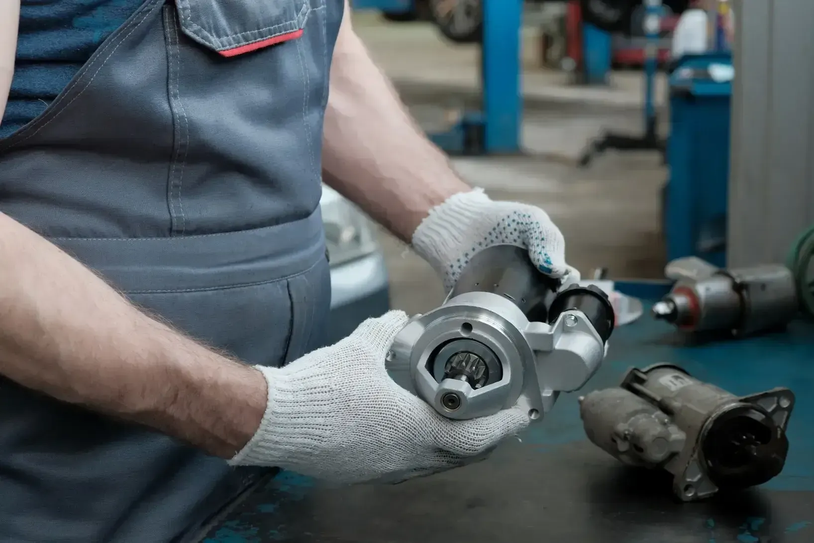 Mechanic in gray gloves inspecting a metal car part on a workshop table