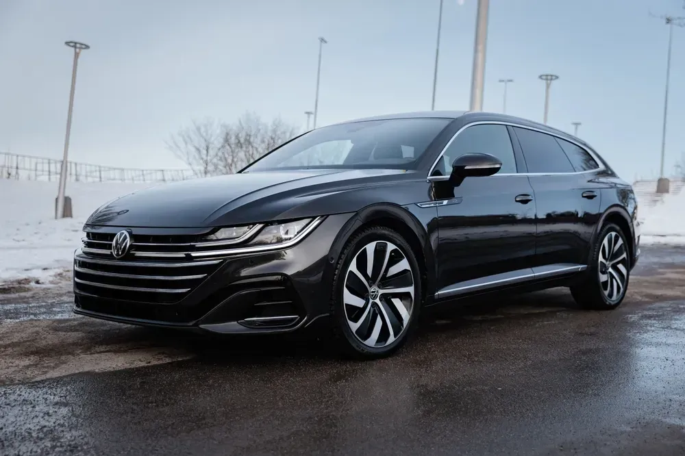 Black Volkswagen sedan parked on a snowy lot on a cloudy day