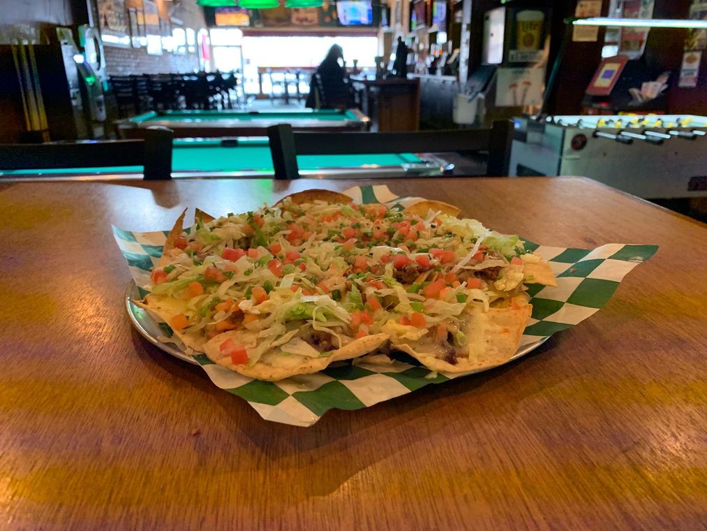 A plate of nachos is sitting on a wooden table in front of a pool table.