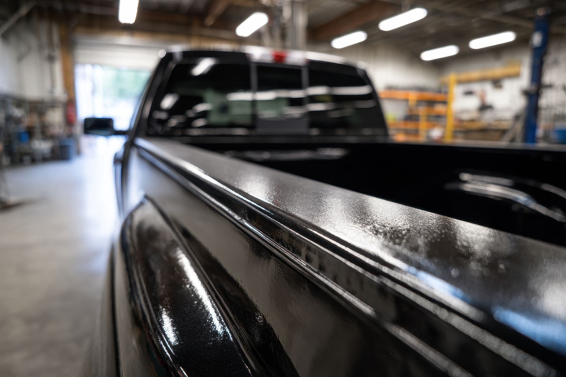 Person in brown coveralls stands between three pickup trucks in a garage, holding a light overhead.